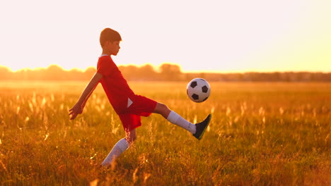 Boy-Junior-in-a-red-t-shirt-and-sneakers-at-sunset-juggling-a-soccer-ball-training-and-preparing-to-become-a-football-player.-The-path-to-the-dream.-Hard-work